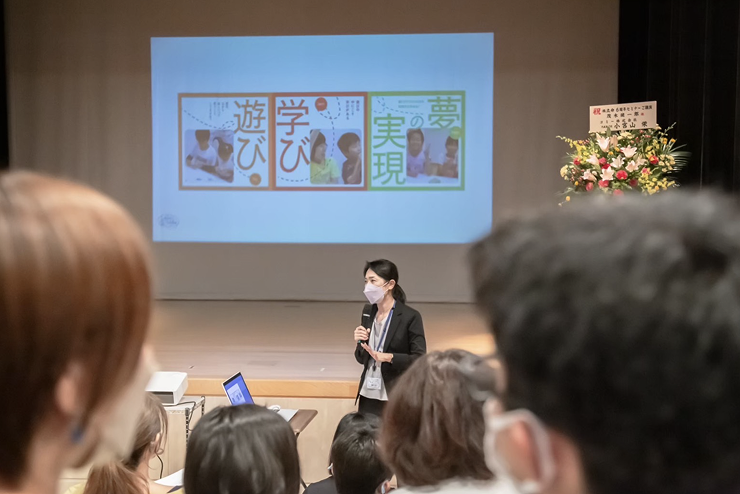大きなホールで塾長の眞野が講演をしている様子